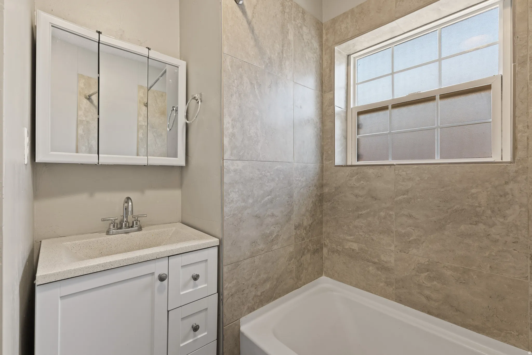 Bathroom featuring a white vanity with integrated sink, chrome faucet, and a mirrored medicine cabinet