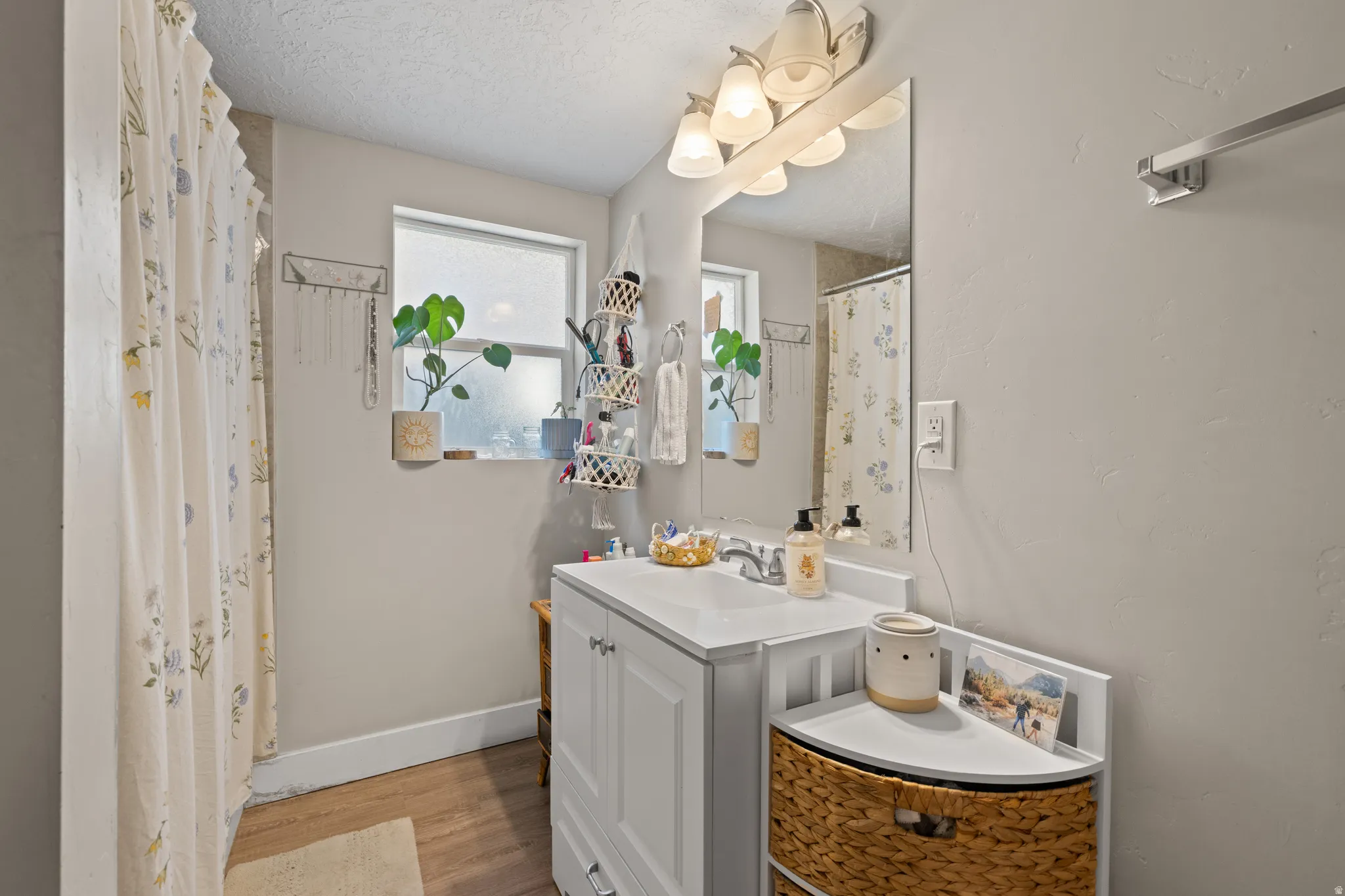 Bathroom featuring wood-finish flooring, a white vanity with a single basin sink, a large wall mirror, and a multi-bulb vanity light fixture