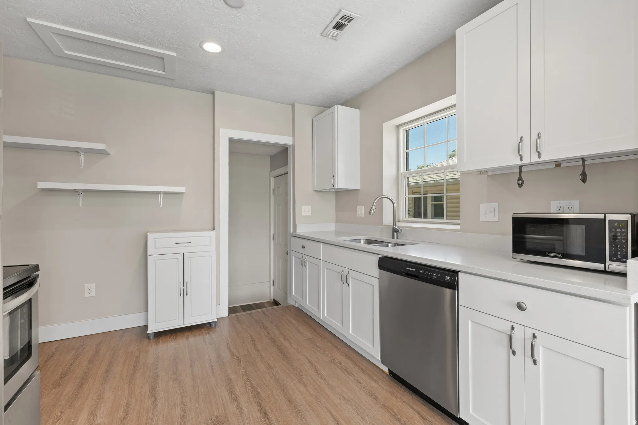 Kitchen featuring wood-finish flooring, white cabinetry, light-toned countertops, and stainless steel appliances