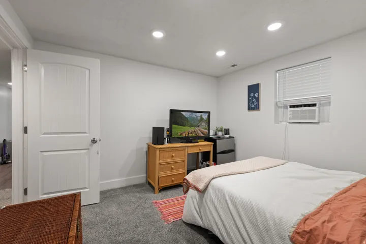 Recessed ceiling lighting illuminates a room featuring gray carpeting, white walls, and a white interior door with paneling