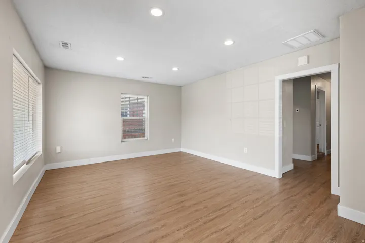 Spacious room featuring wood-finish flooring, recessed ceiling lighting, and multiple windows with blinds