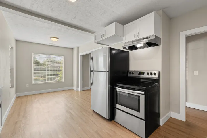 Kitchen area with stainless steel appliances, white cabinetry, and wood-finish flooring