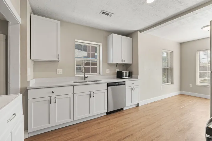 Kitchen featuring white shaker cabinetry, stainless steel dishwasher, undermount sink with gooseneck faucet, light-toned countertops, and wood-finish flooring