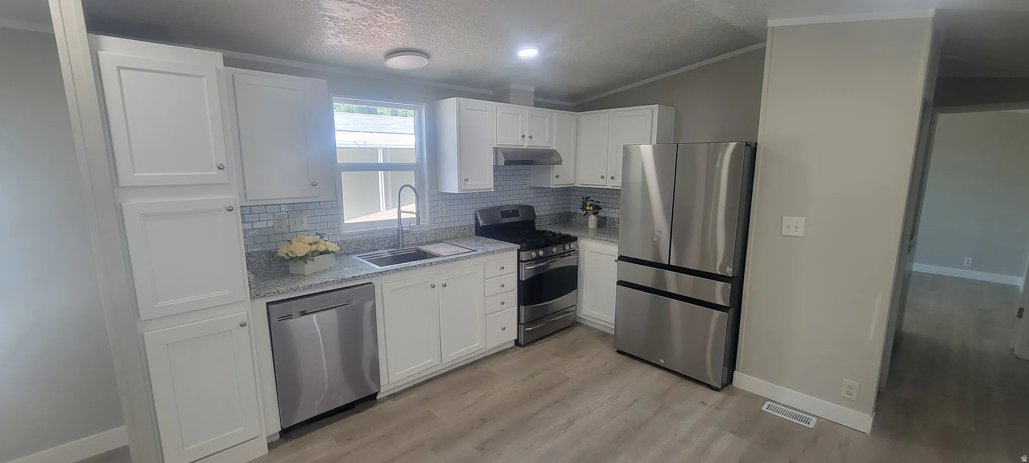 Modern kitchen featuring white shaker-style cabinetry, stainless steel appliances, speckled countertops, a subway tile backsplash, and light wood-finish flooring