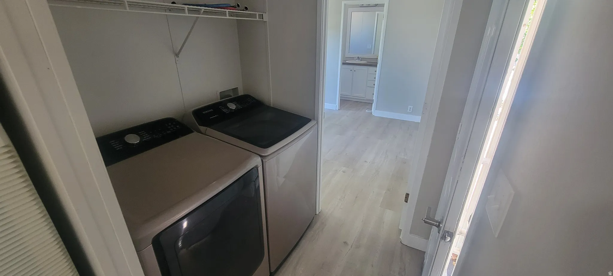 Laundry area with built-in wire shelving and light wood-finish flooring extending into the hallway