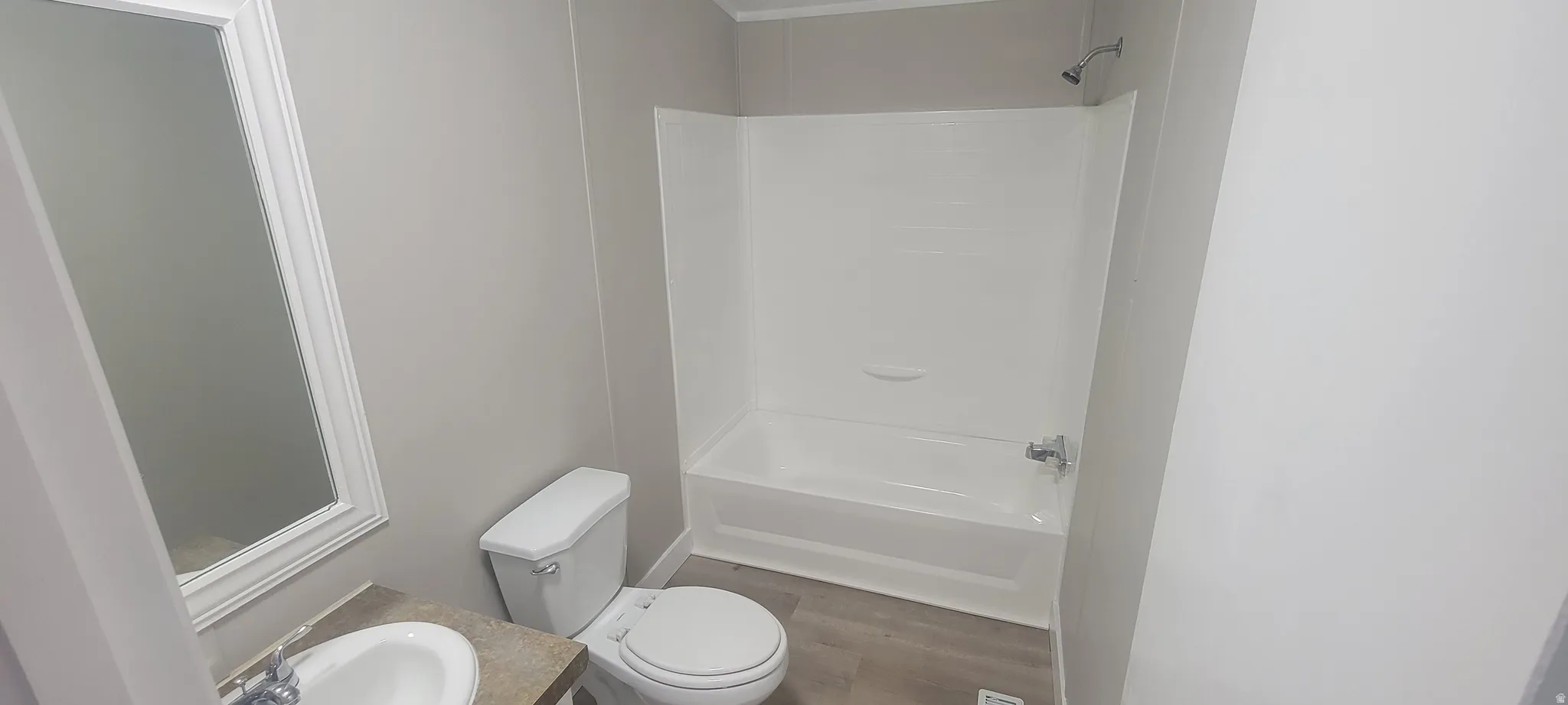 Bathroom featuring a white tub and shower combination with a single showerhead, a white toilet, and a vanity with a drop-in sink and a framed mirror