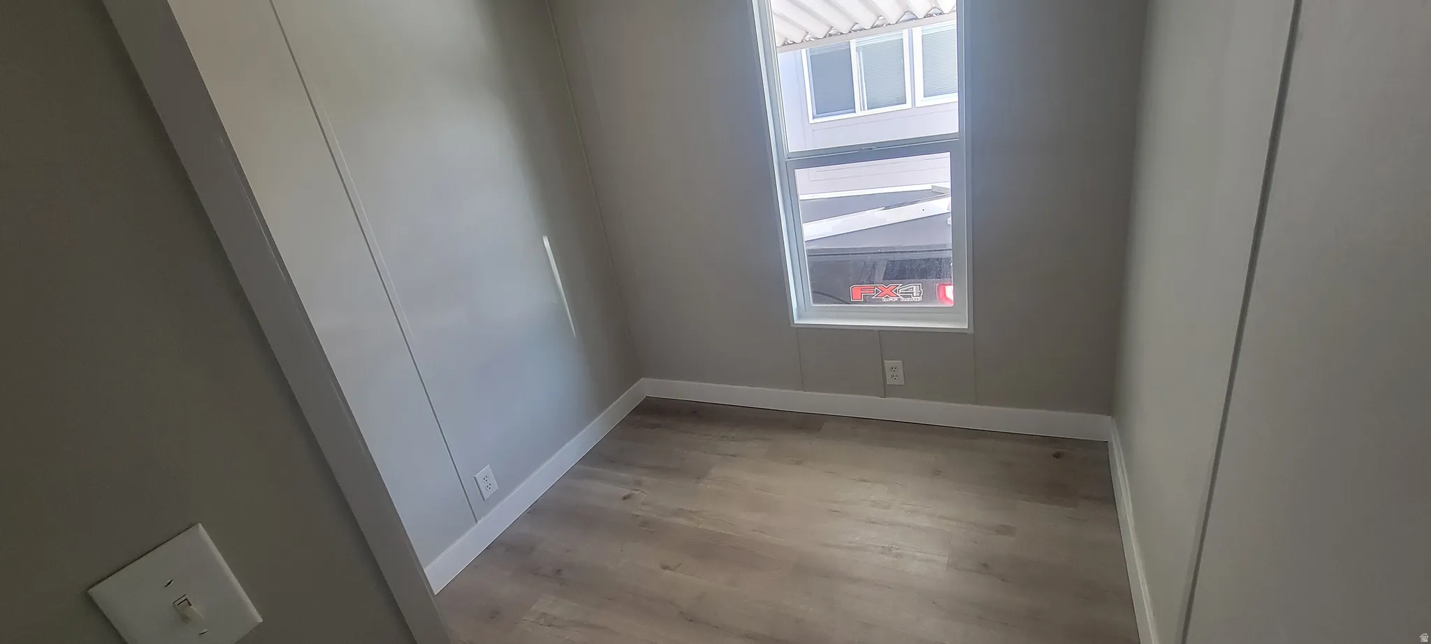 Room featuring a single window, light wood-finish flooring, light gray walls, white baseboards, and white trim