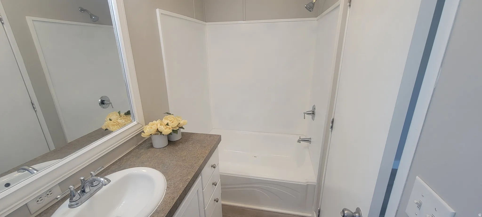 Bathroom featuring a white bathtub and shower combination with chrome fixtures, a vanity with a drop-in sink, a stone-finish countertop, and a large framed mirror