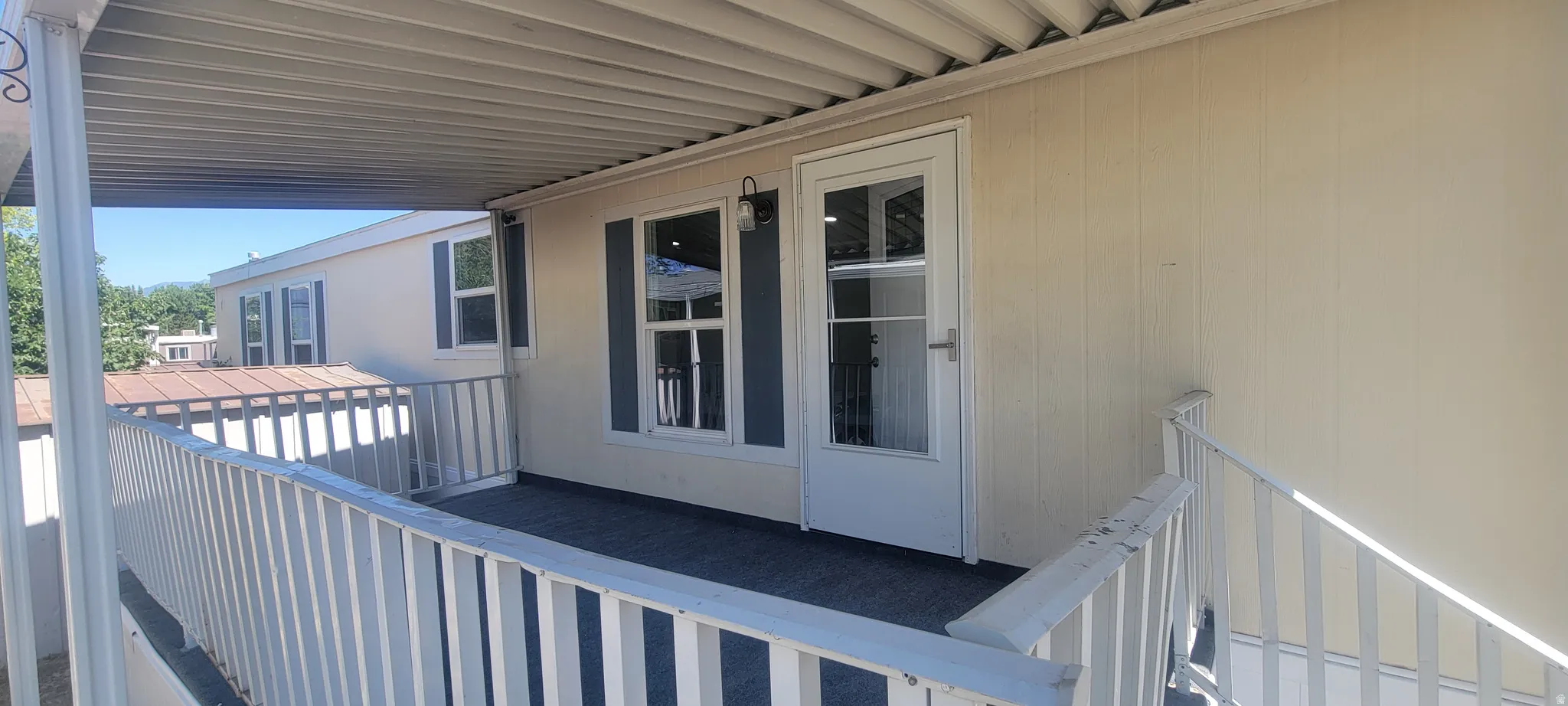Covered porch with durable outdoor carpeting, white railing, and exterior wall lantern