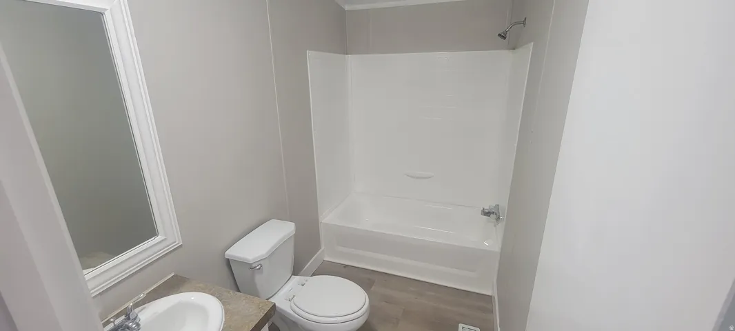 Bathroom featuring a white tub and shower combination with a single showerhead, a white toilet, and a vanity with a drop-in sink and a framed mirror