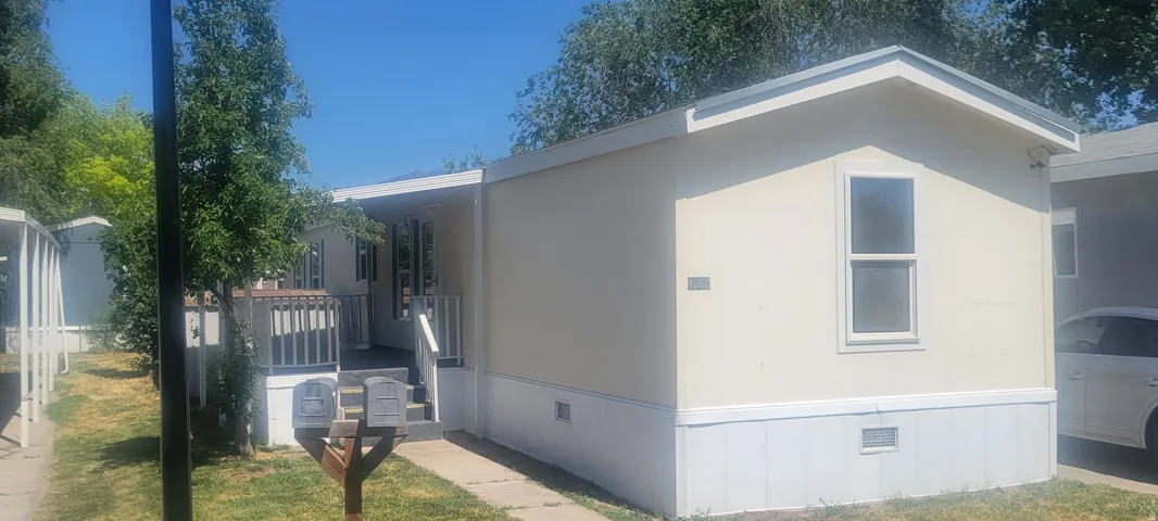 Exterior featuring light-colored siding with white trim, a covered porch with wood railing, and a concrete walkway