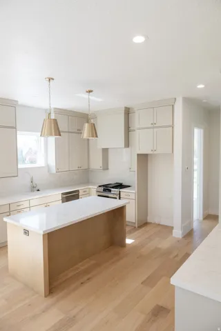 Gourmet kitchen featuring a large central island with a solid surface countertop, light wood-finish flooring, recessed lighting, and stylish pendant light fixtures