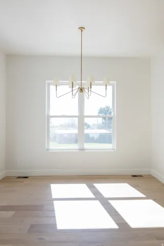 Bright room featuring a multi-pane window, a brass chandelier, wood-finish flooring, and white baseboards