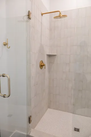Glass-enclosed shower featuring a brass rain showerhead, brass faucet, and a built-in shower niche