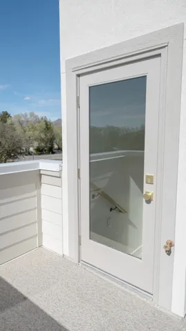 Exterior balcony with textured surfacing, white siding, and a full-light door with brass hardware