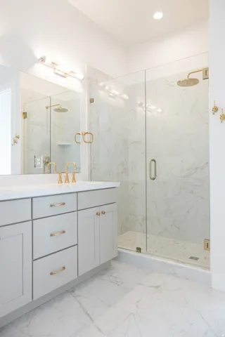 Spacious bathroom featuring a glass-enclosed shower with gold-tone fixtures and a rainfall showerhead