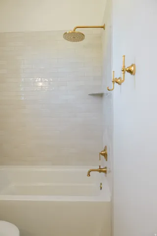 Bathtub and shower combination featuring a rain shower head, subway tile surround, brass fixtures, and an integrated shower shelf