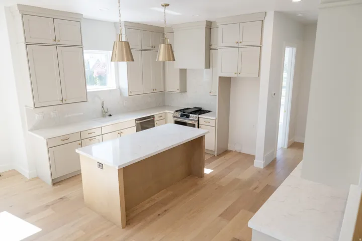 Contemporary kitchen featuring a central island with a light wood base and a light-toned countertop, complemented by perimeter cabinetry with light-colored shaker-style doors and brass-toned hardware