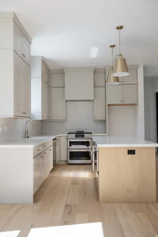 Kitchen featuring light wood-finish flooring, white perimeter cabinetry with brass hardware, stainless steel double oven range, and a white countertop island with integrated power outlets