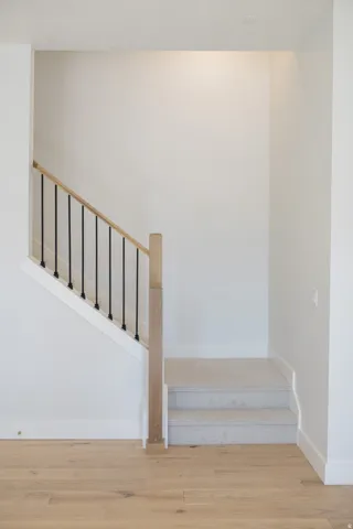 Modern staircase featuring a light wood-finish handrail, black metal balusters, and light carpeted steps