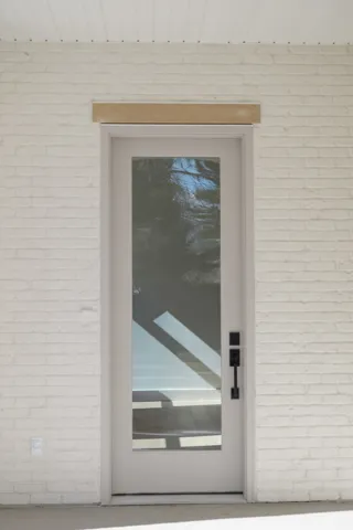 Modern entry door with full-lite glass panel, matte black hardware, and an overhead transom
