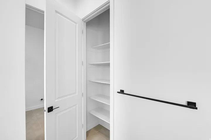 Utility closet with multiple white shelves, a contrasting black hardware door handle, and a black towel bar