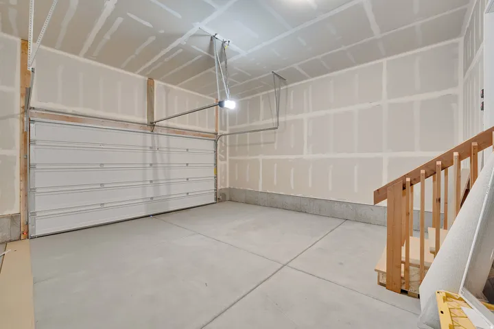 Spacious garage featuring a concrete floor, an overhead door, and exposed wood stairs