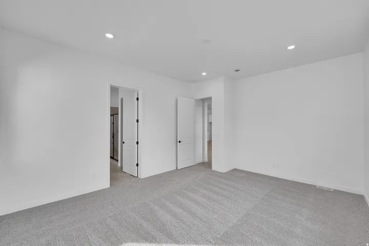Spacious room featuring neutral carpeting, white walls, recessed lighting, and white interior doors with dark hardware