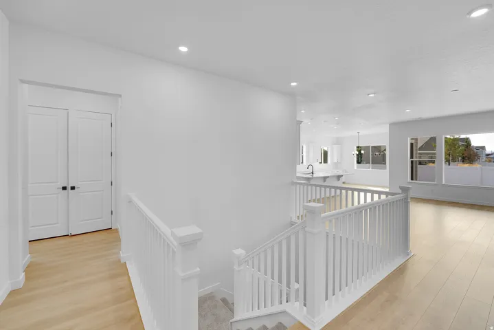 Bright interior featuring light wood-finish flooring, white walls, recessed lighting, white railing, and white double doors with black hardware