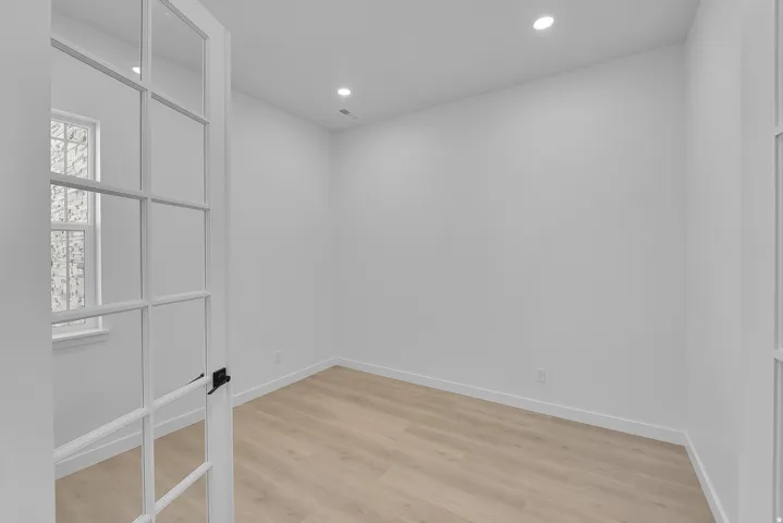 French doors with dark hardware open into a room featuring light wood-finish flooring, recessed lighting, and white baseboards