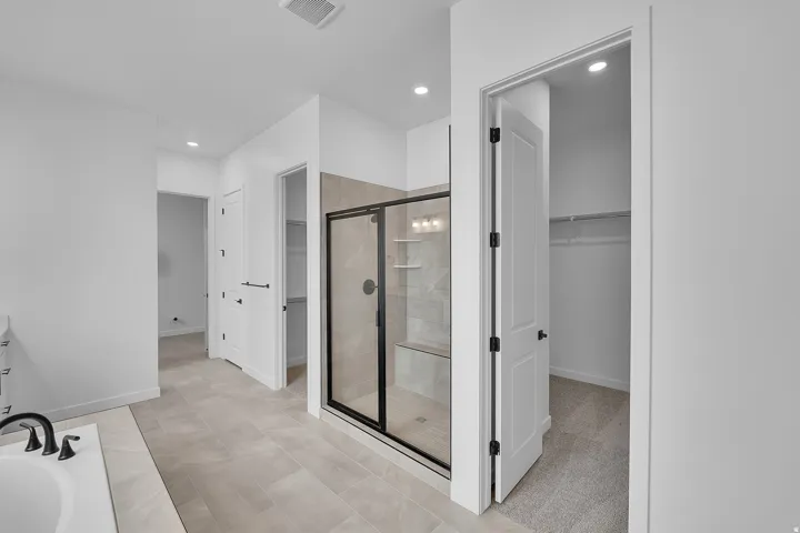 Spacious bathroom featuring a glass-enclosed shower with tile surround and built-in shelving, a deep soaking tub with matte black fixtures, and light-toned tile flooring