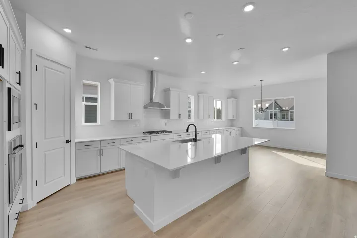 Spacious kitchen featuring an expansive central island, white cabinetry with black hardware, integrated double ovens, and wood-finish flooring