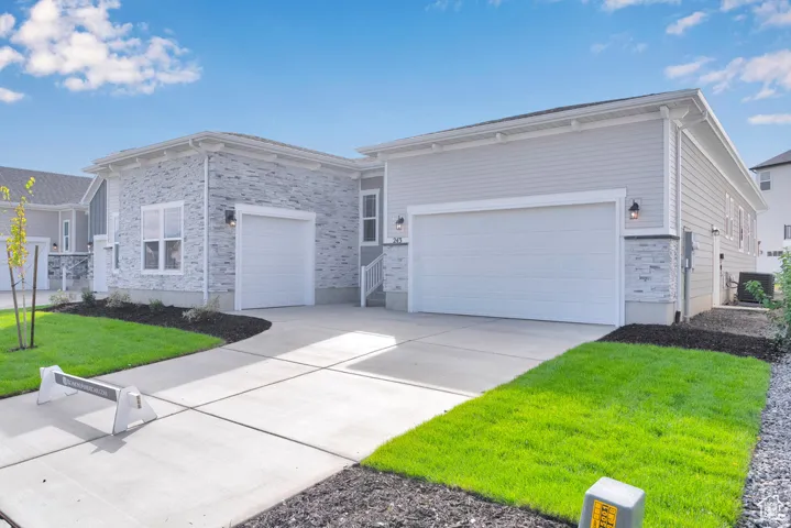 Light gray siding exterior with stone accents, two white garage doors, a concrete driveway, and manicured lawns