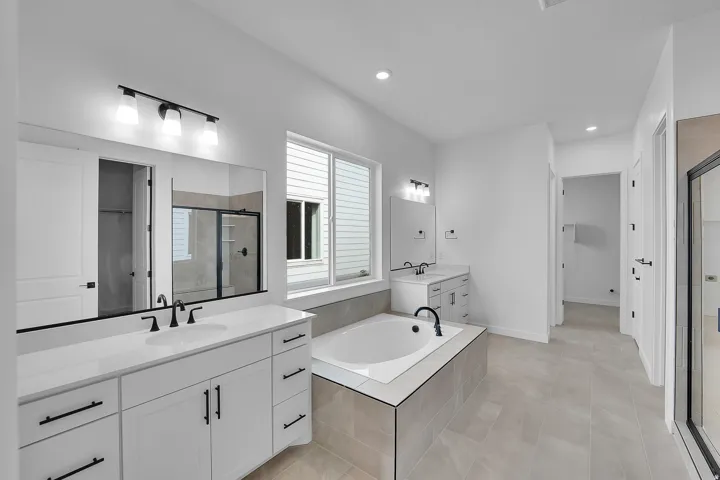 Spacious bathroom featuring a built-in soaking tub with a tiled surround, dual vanity areas, and a large window providing natural light