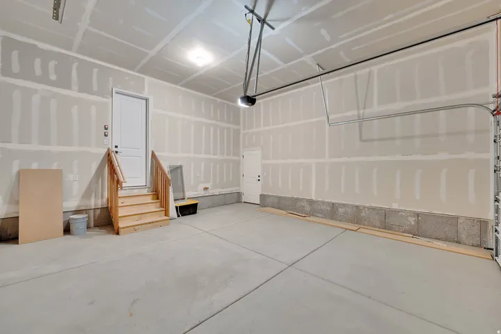 Spacious garage featuring concrete flooring, an interior access door with wooden stairs and railing, overhead lighting, and an automatic garage door opener