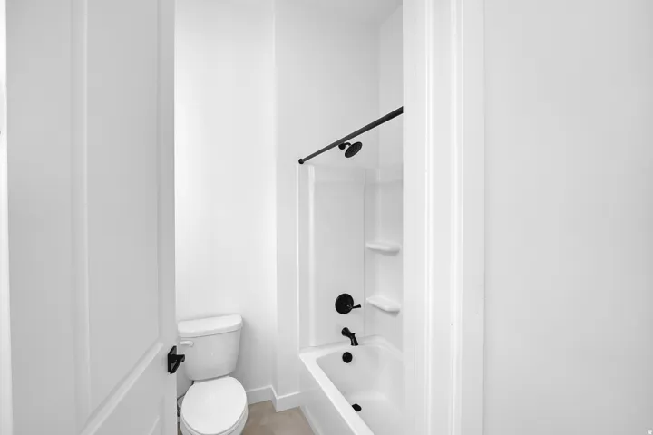 Bathroom featuring a white tub and shower combination with matte black fixtures, a white toilet, and light-colored flooring