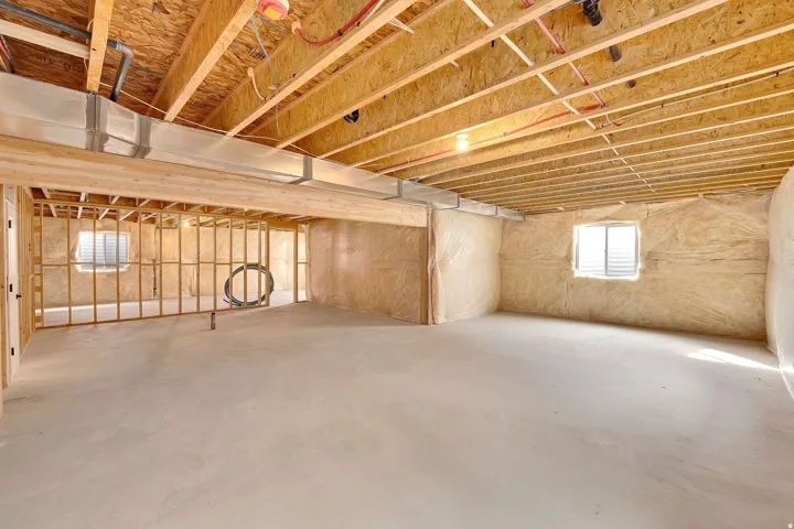 Unfinished basement featuring exposed wood joists and subflooring, concrete flooring, framed wall sections, and two visible windows