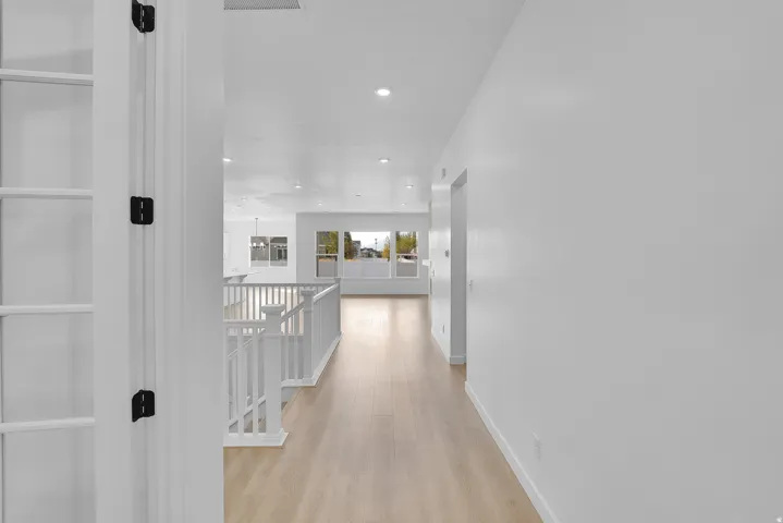 Bright hallway featuring light wood-finish flooring, recessed lighting, and a white baluster railing