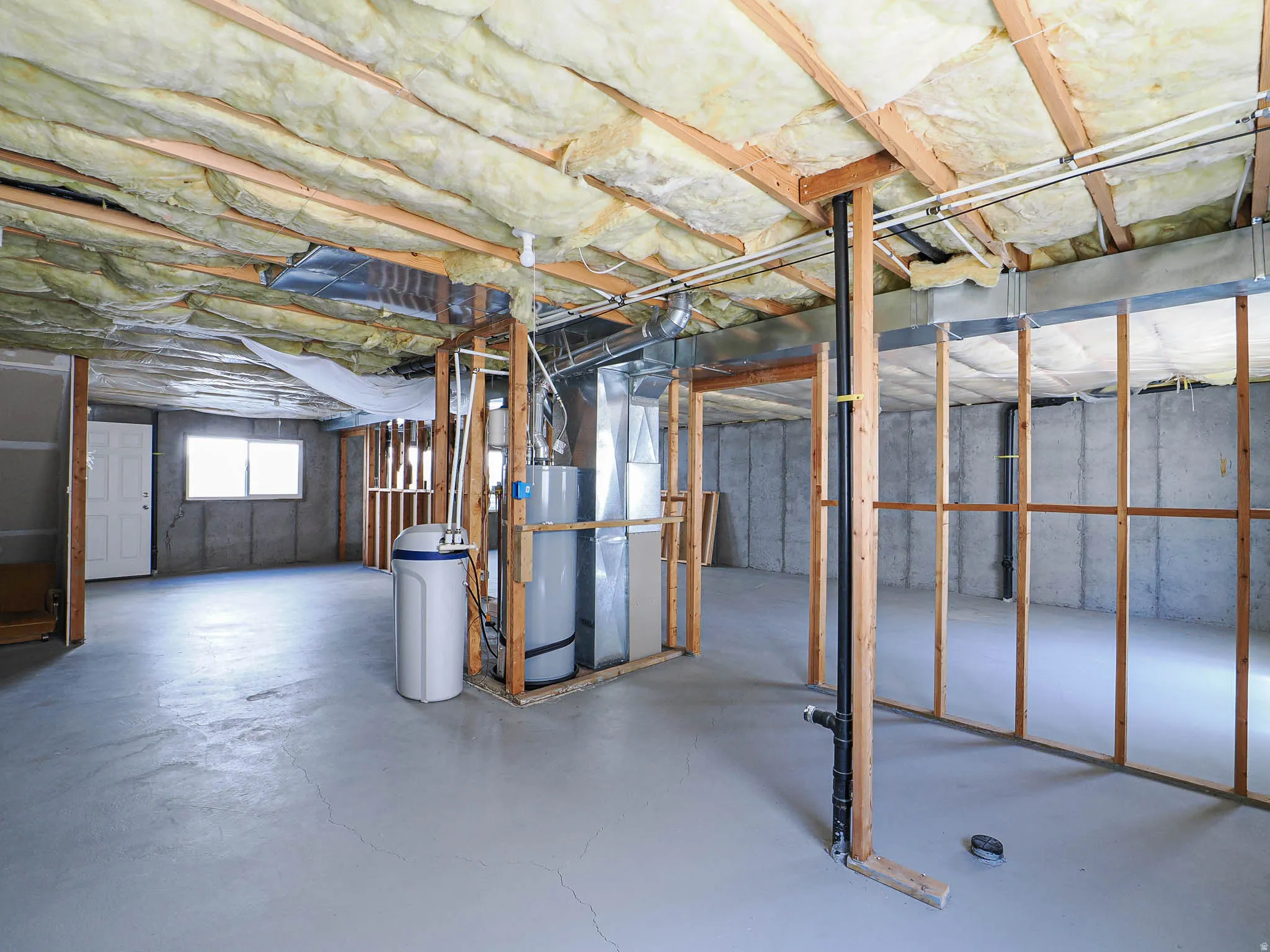 Unfinished basement featuring exposed ceiling joists with insulation, concrete slab flooring, and structural wood framing