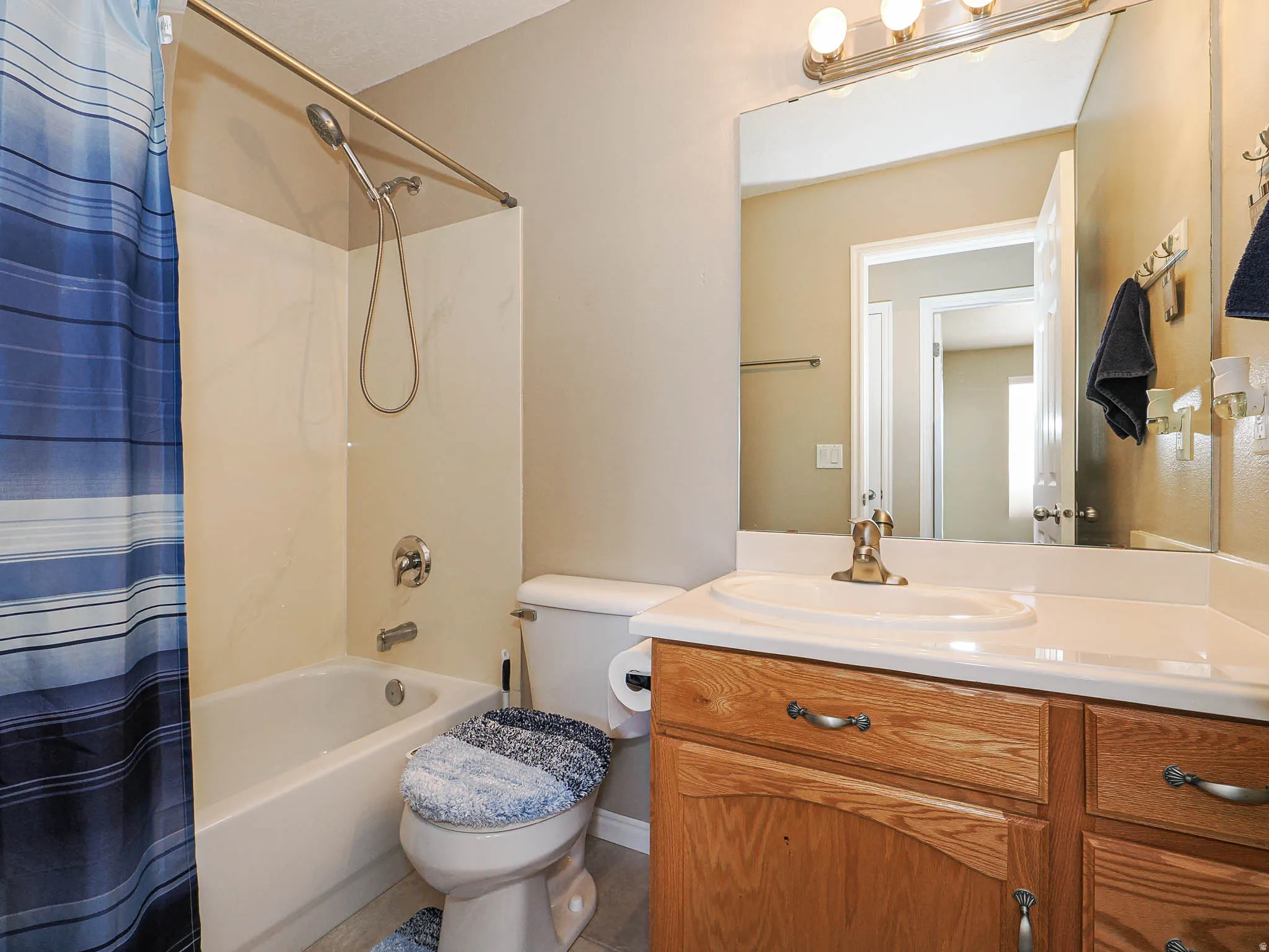 Bathroom featuring a white bathtub with a shower kit, a toilet, a vanity with a white countertop and integrated sink, and wood-finish cabinetry