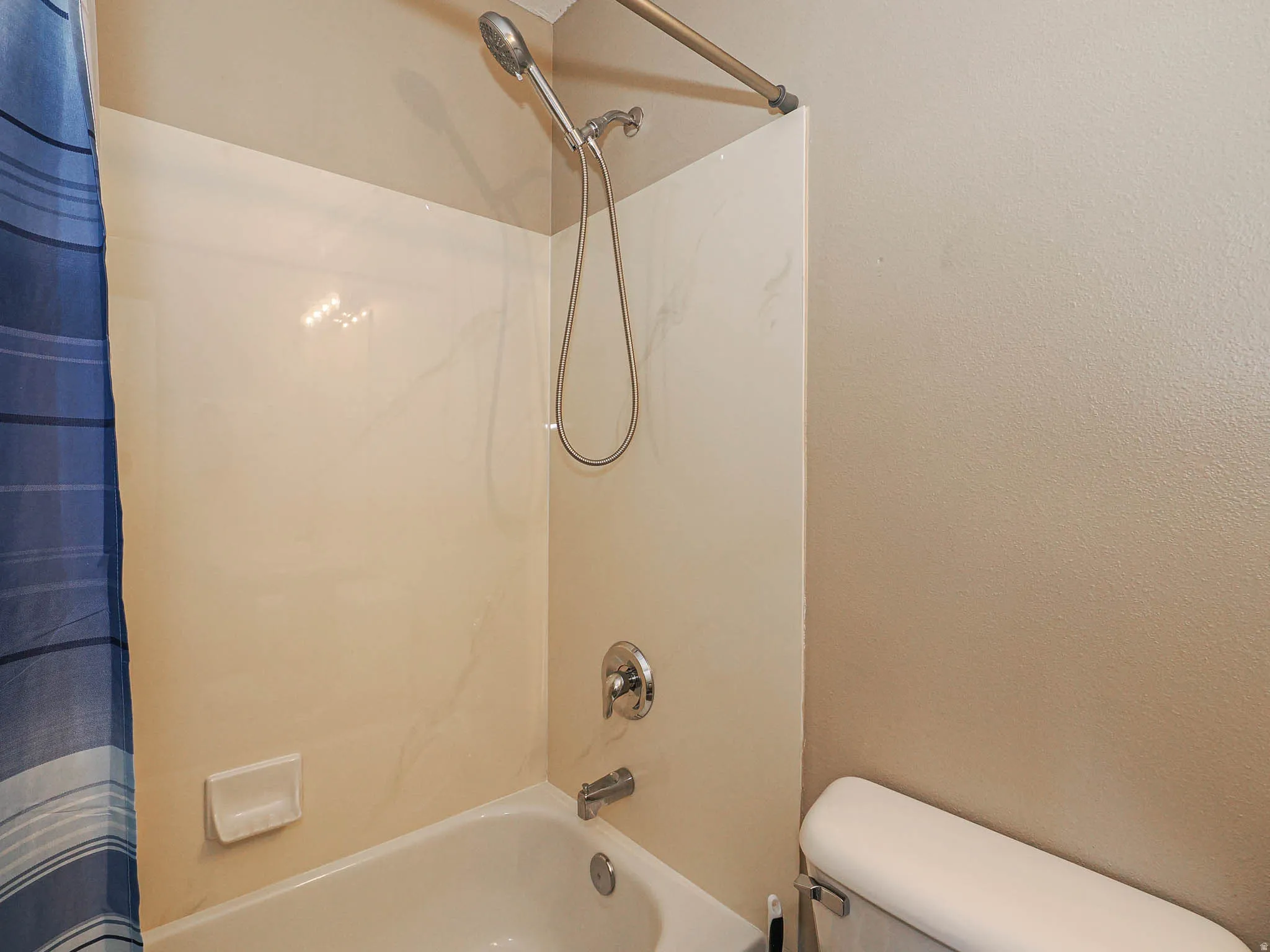 Tub and shower combination featuring a curved shower rod, handheld shower fixture, and a tile-look surround