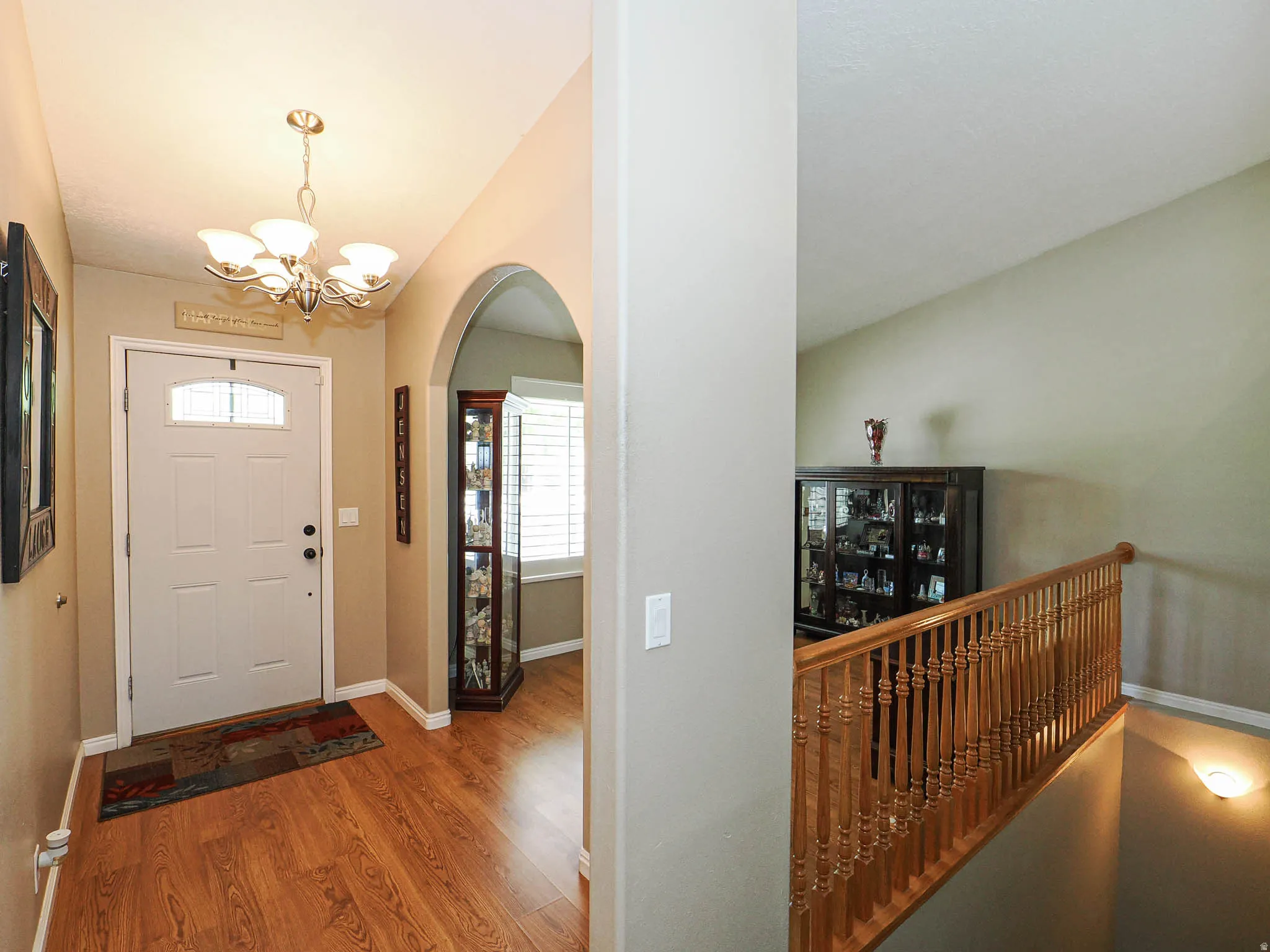 Foyer entry featuring wood-finish flooring, a contemporary chandelier, arched doorway, and a white front door with decorative glass inserts