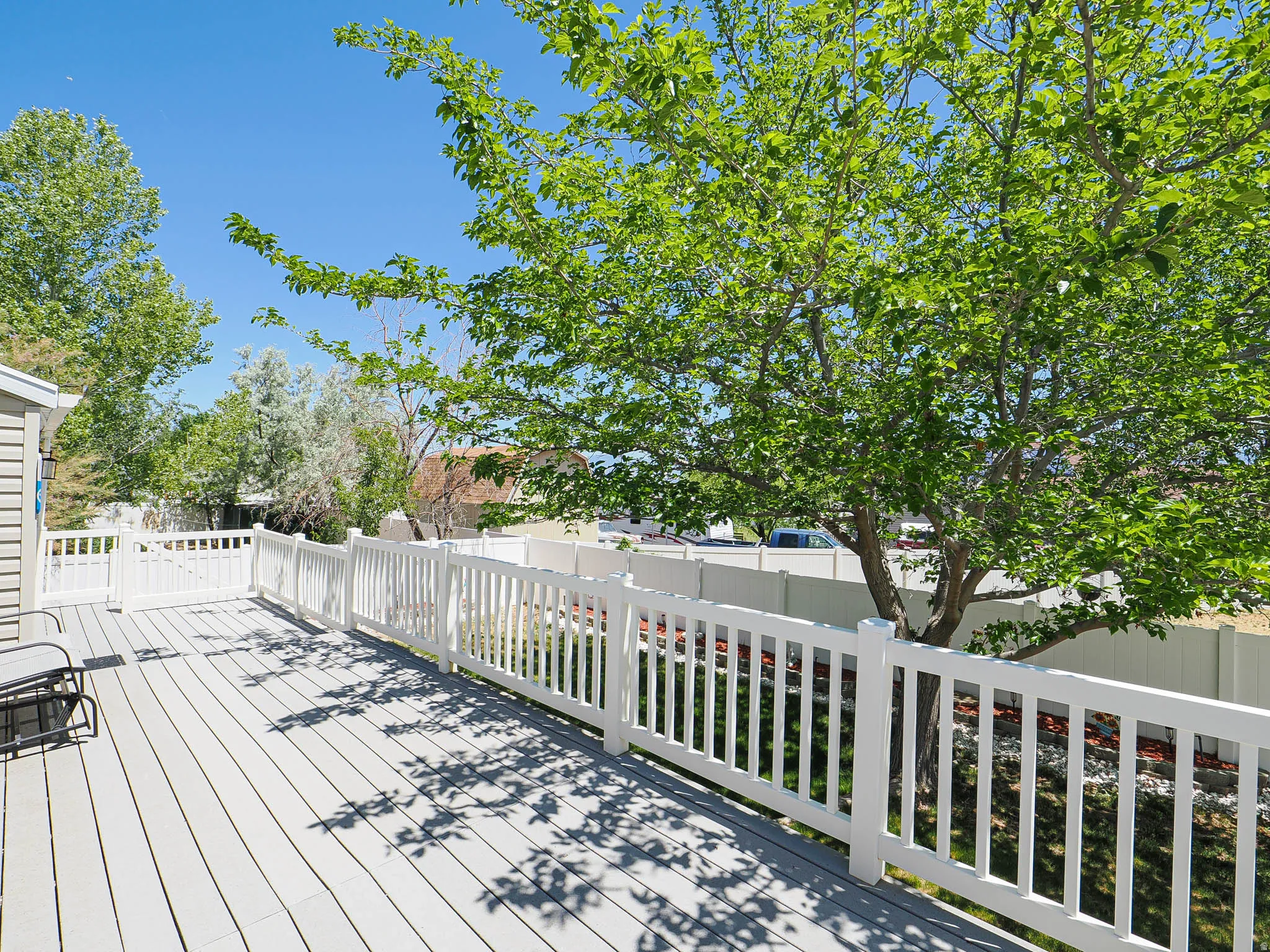 Expansive outdoor deck featuring light gray composite decking, white railings, and mature trees providing natural shade