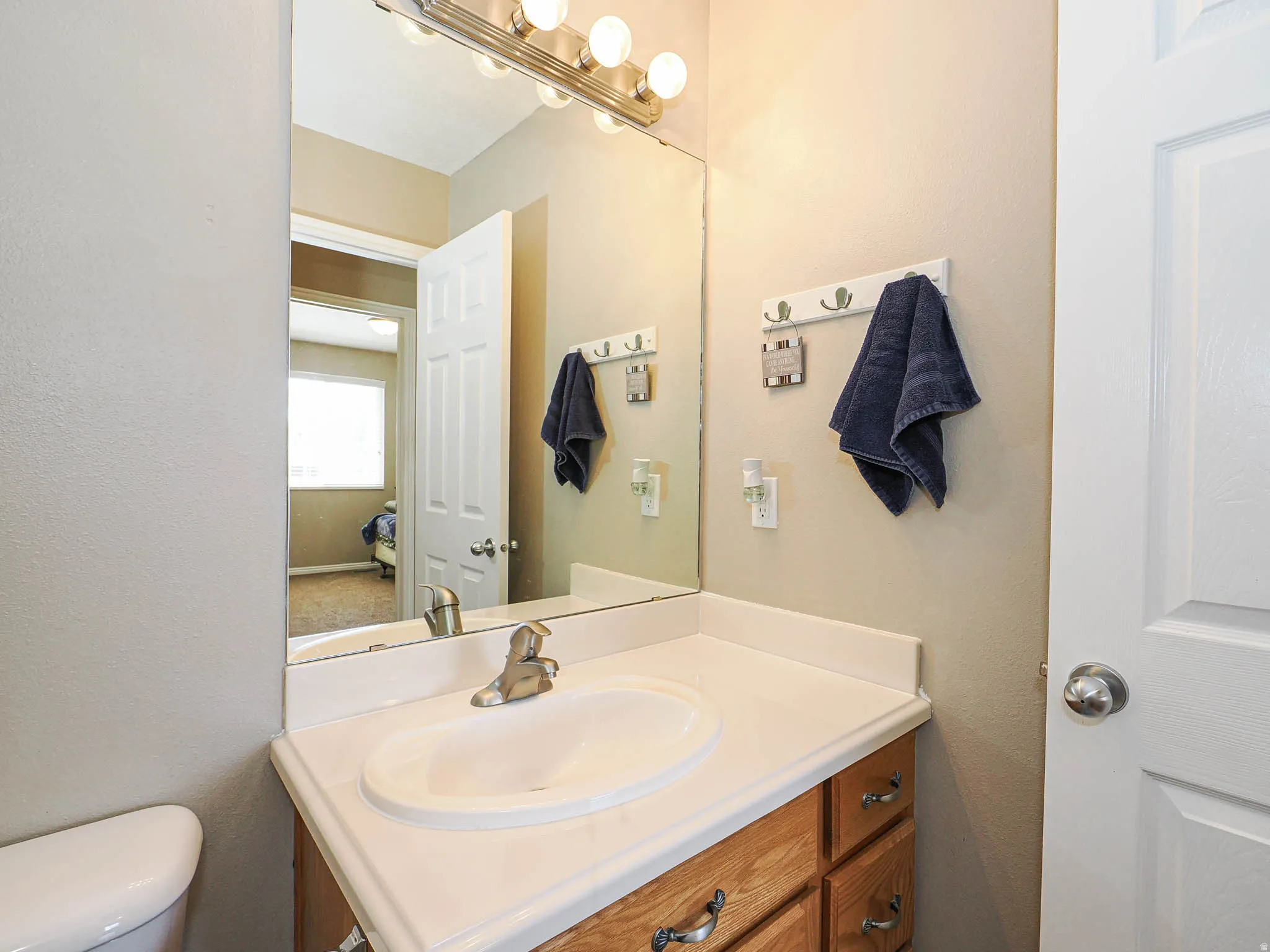 Bathroom vanity featuring a white countertop with an integrated sink, wood-finish cabinetry with silver-tone hardware, and a large mirror with overhead vanity lighting