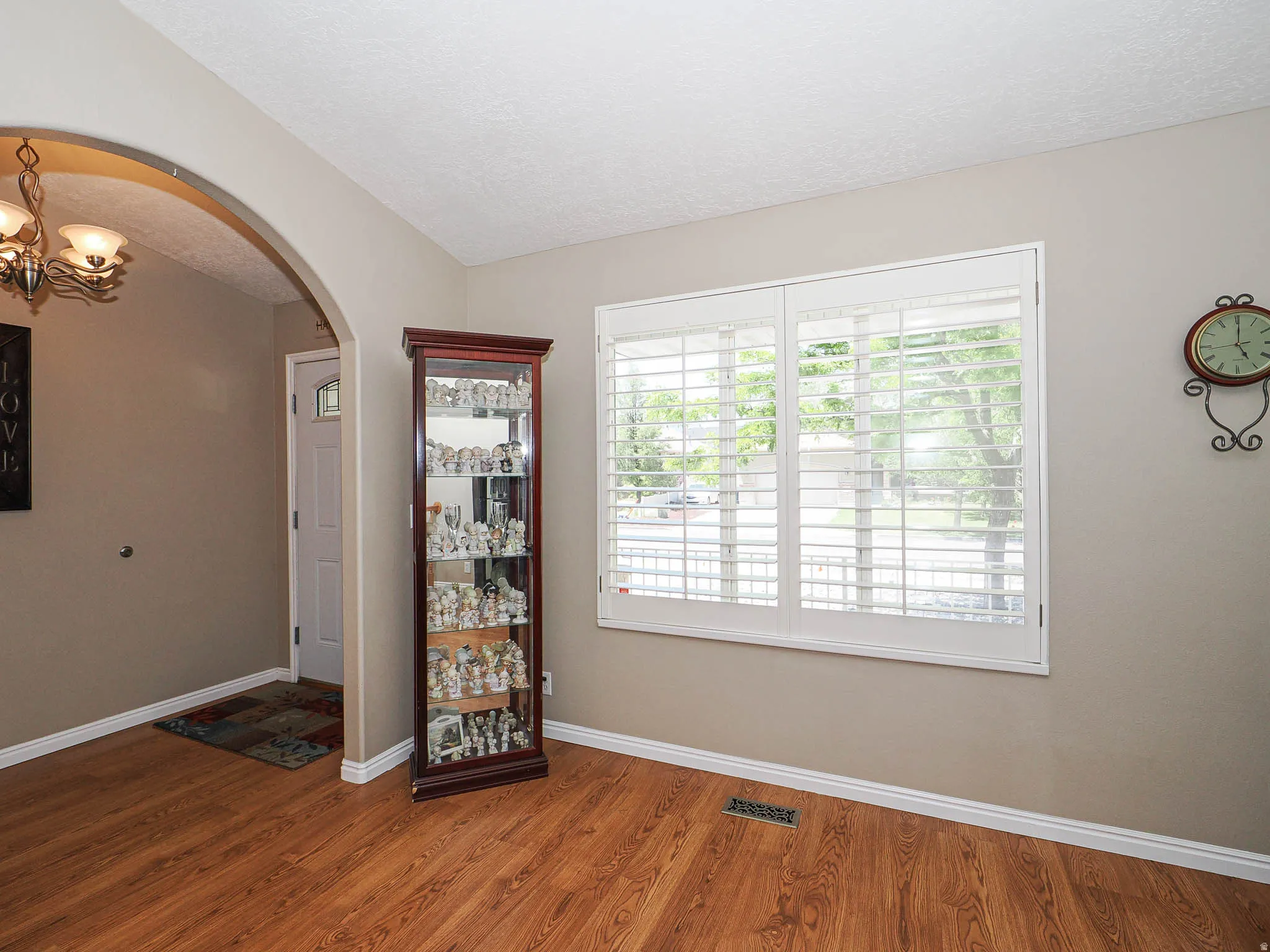 Spacious interior with wood-finish flooring, plantation shutters, and an arched entryway