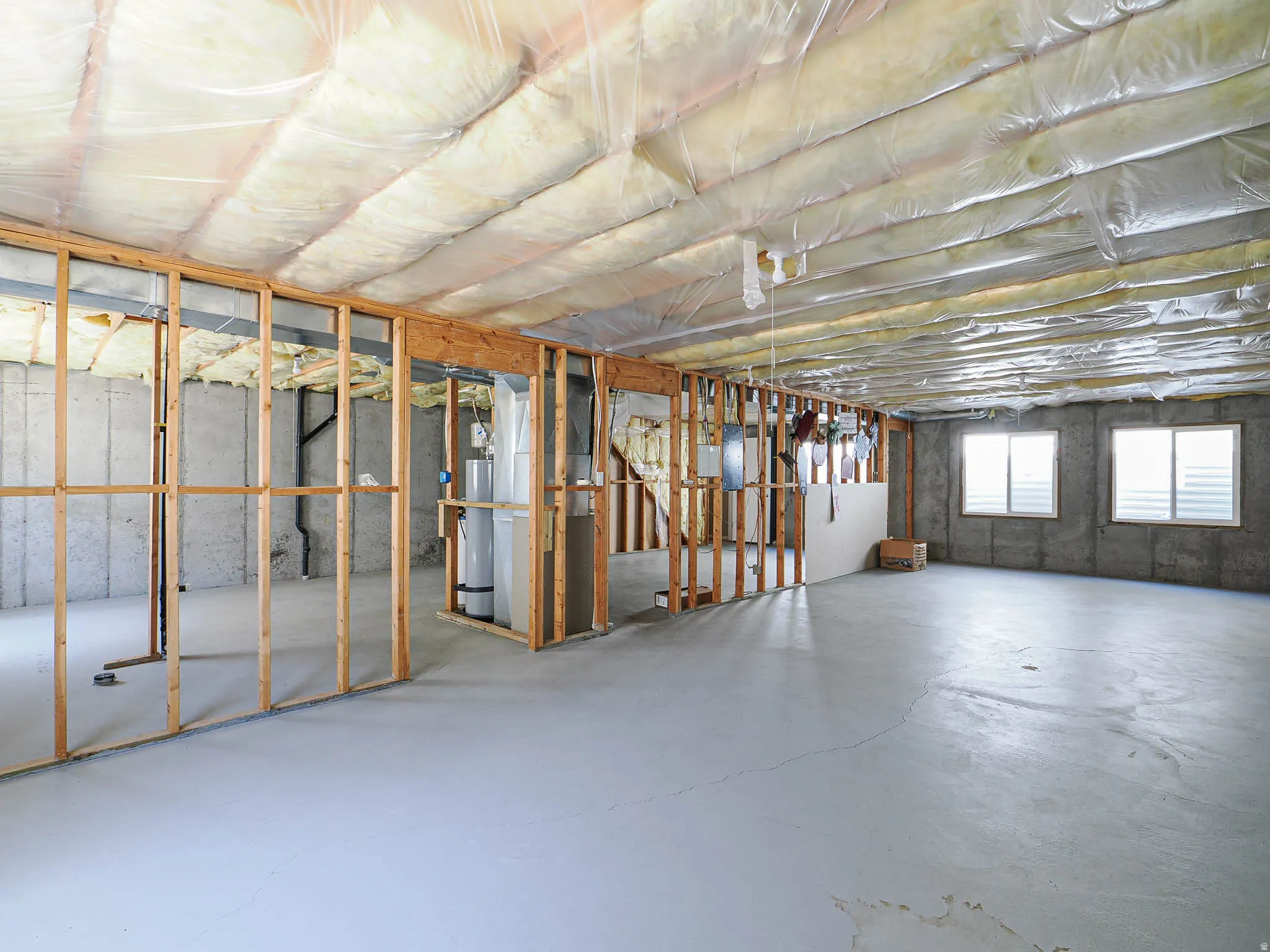 Unfinished basement featuring concrete walls, concrete flooring, two windows, wood framing, and ceiling insulation