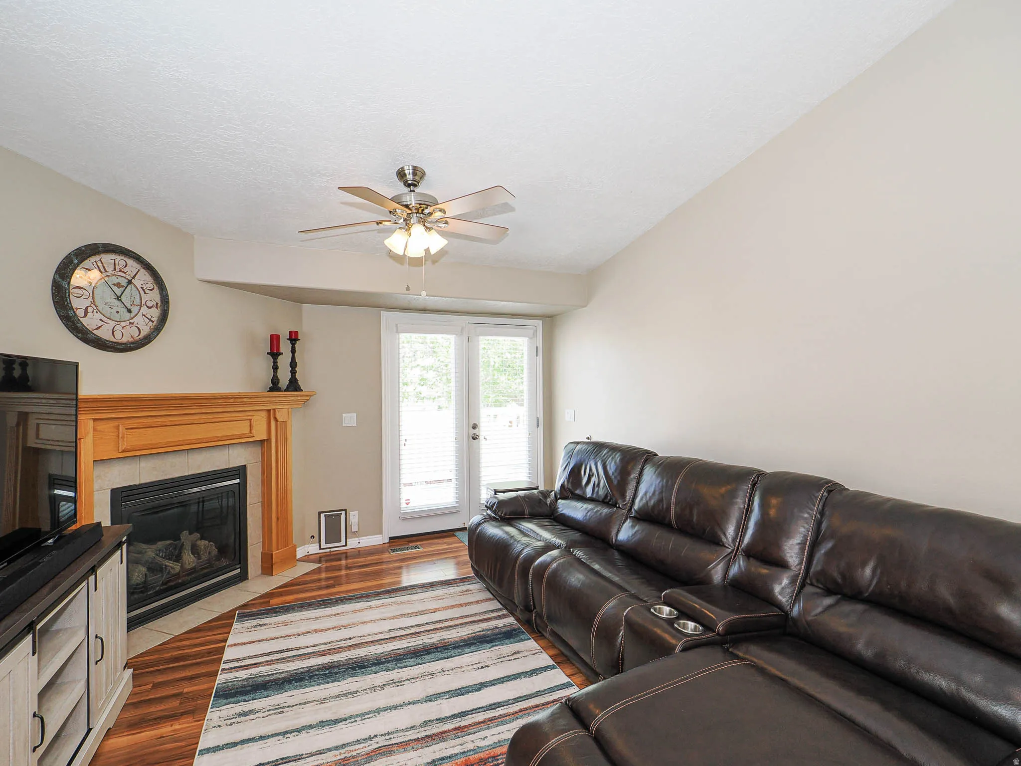 Living space featuring a natural wood mantelpiece above a fireplace with a tile hearth, wood-finish flooring, and a vaulted ceiling with a ceiling fan