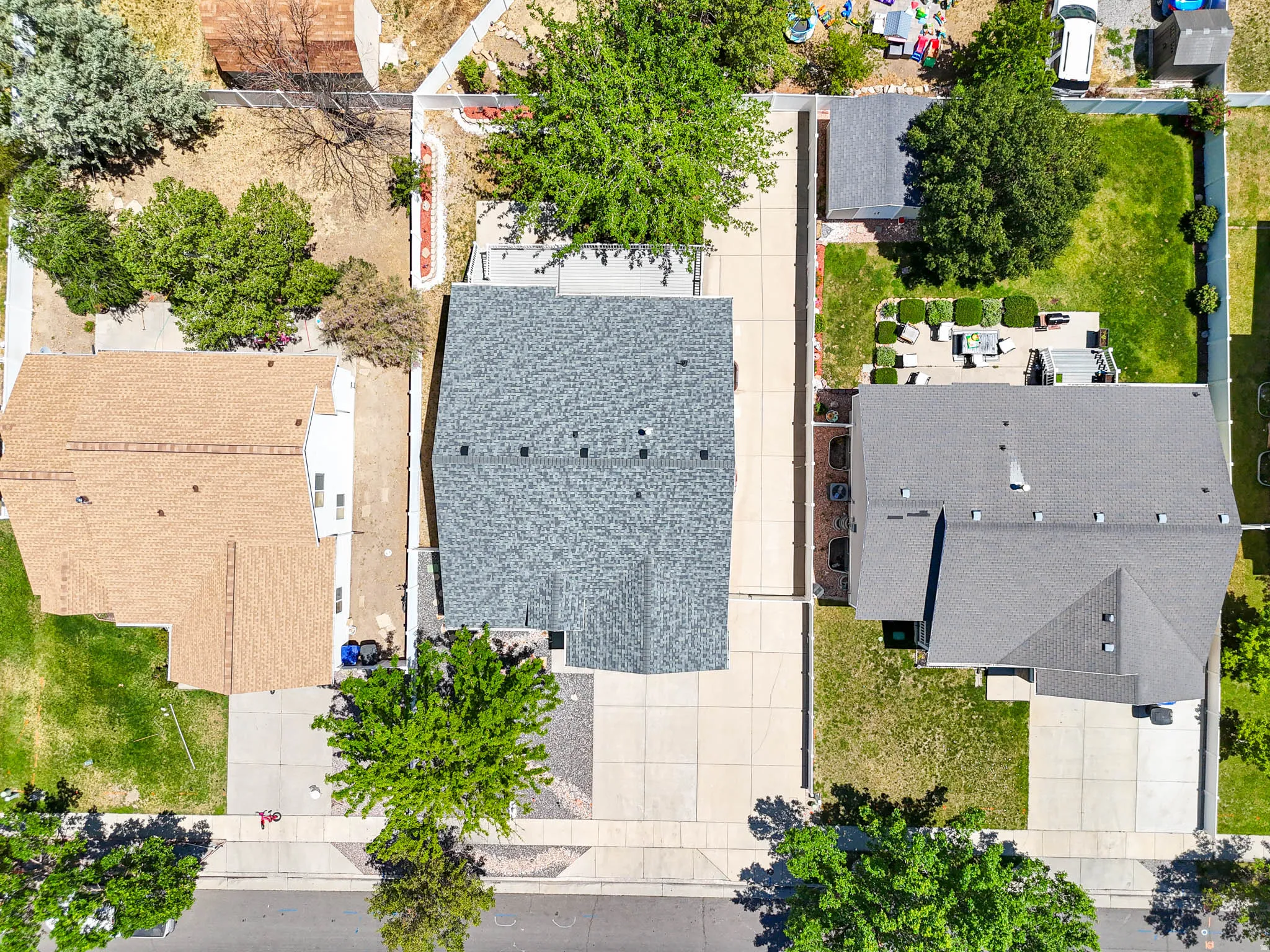Aerial perspective showcasing a property with a grey shingle roof, a paved driveway, and a backyard featuring a patio area with outdoor furniture