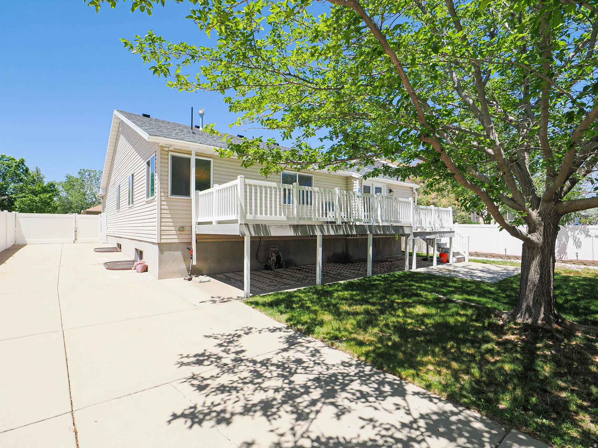 Rear exterior featuring light-colored siding, a multi-level deck with white railings, and a concrete patio below