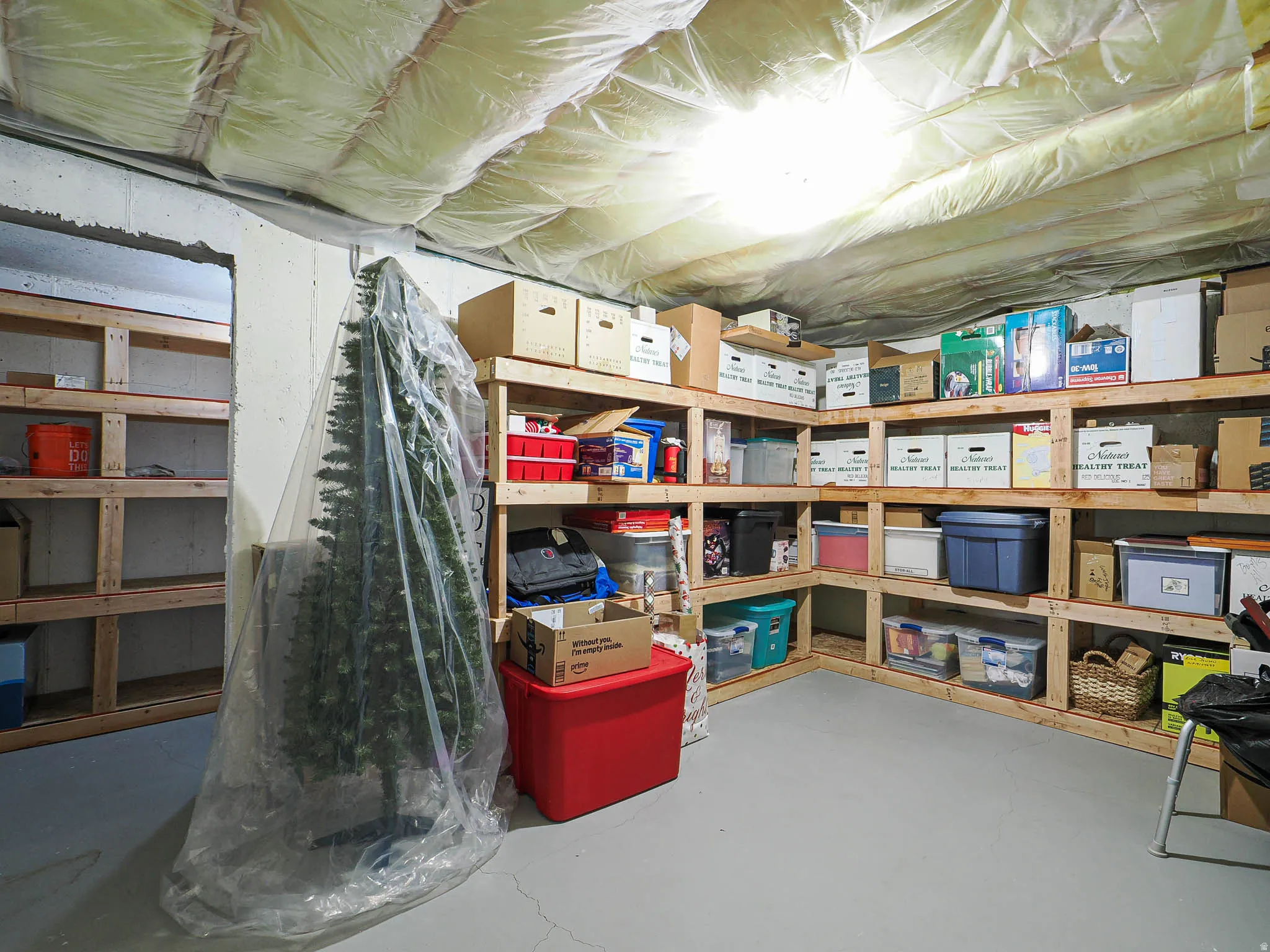 Basement storage area featuring extensive built-in wooden shelving, concrete block walls, and a painted concrete floor